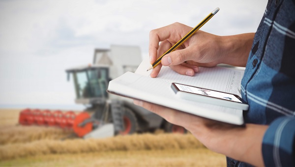 A farmer stands in front of a tractor with a clipboard