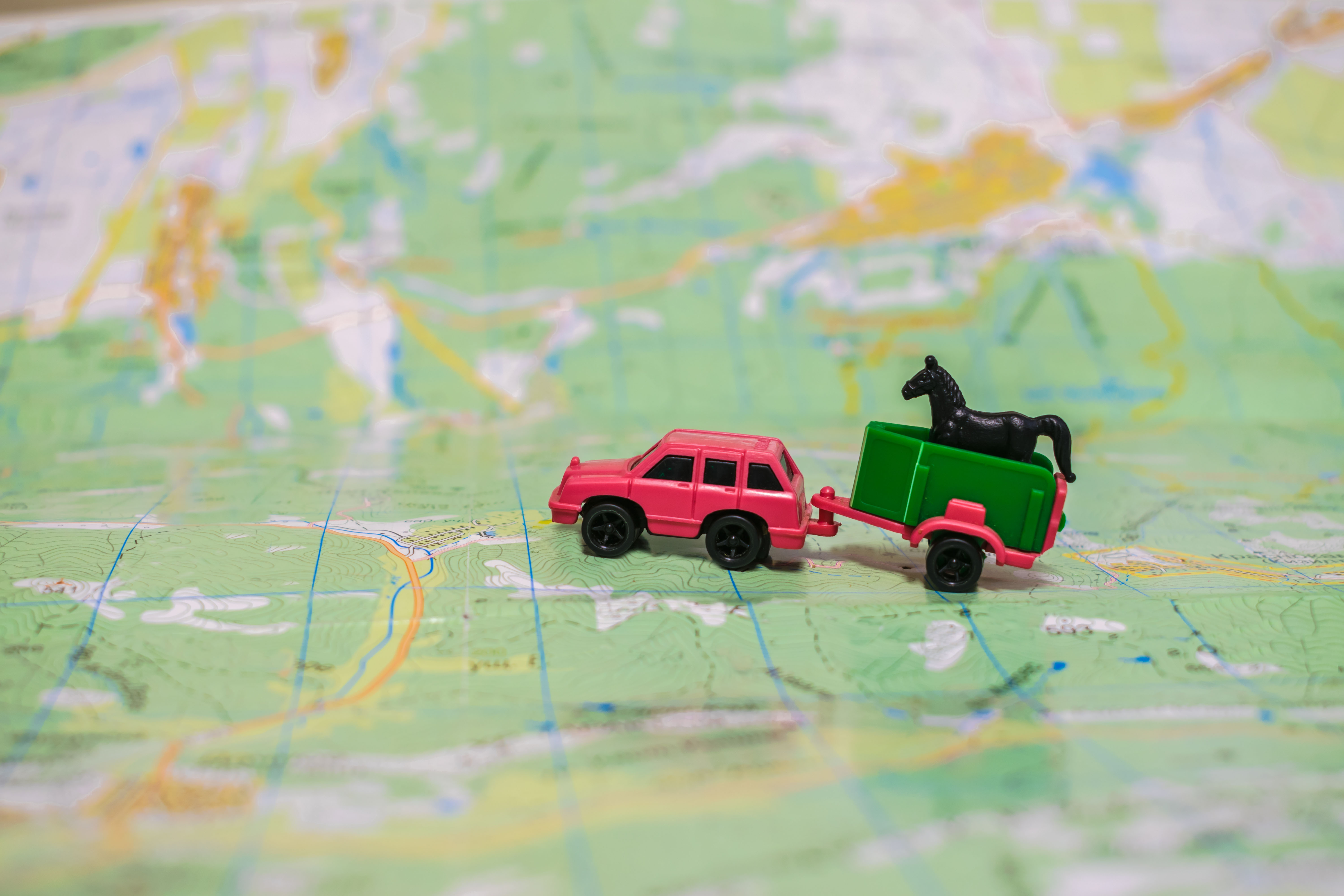 Toy car towing a trailer with toy horse across a map