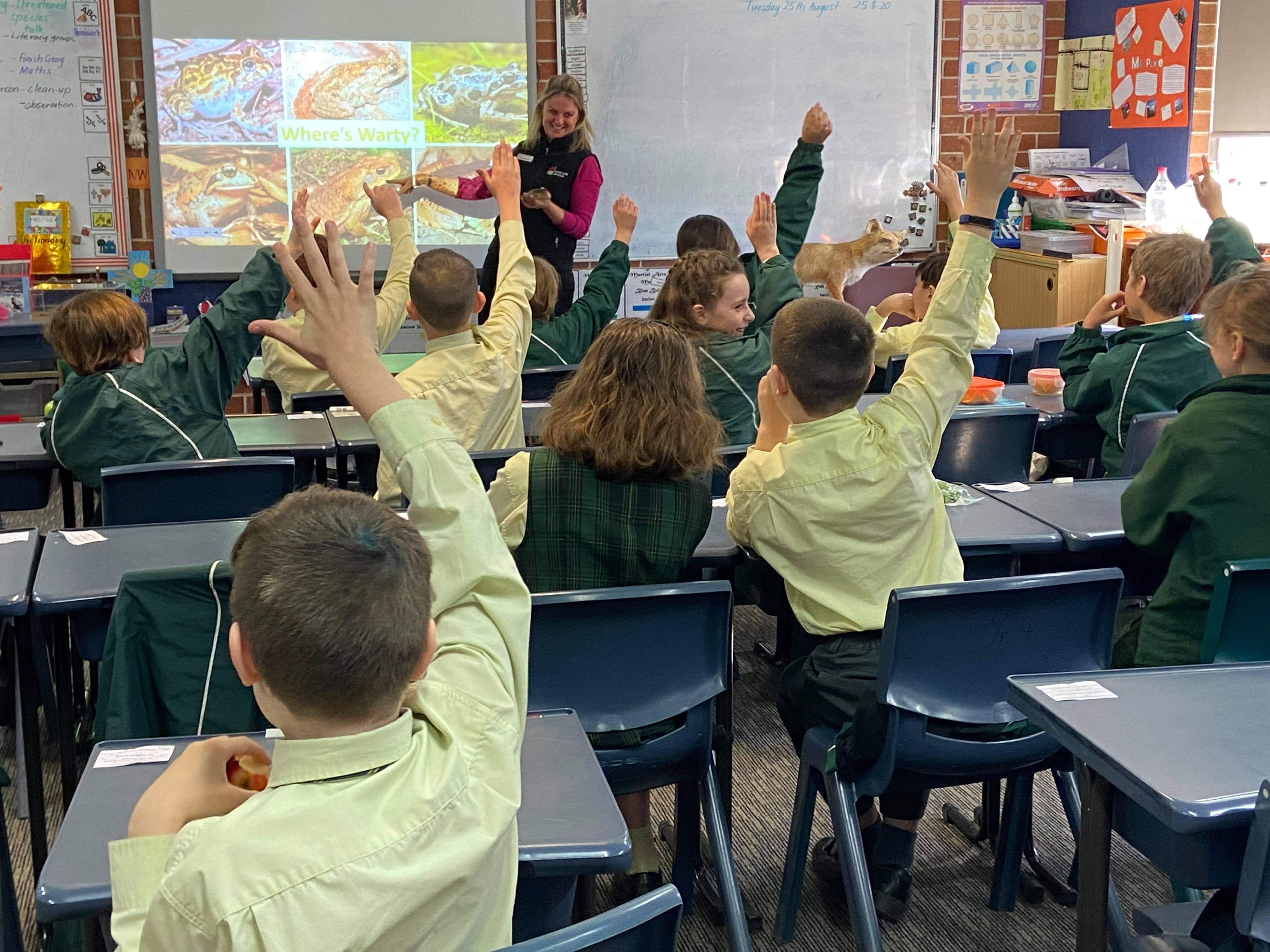 A group of children with their hands up in a classroom