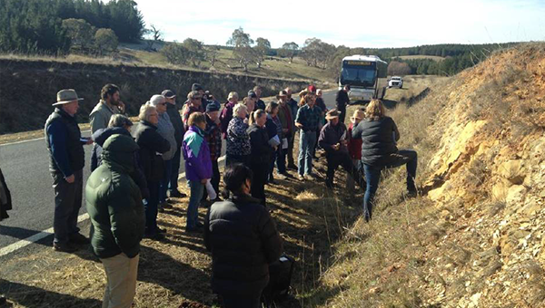 A group of people standing on the side of a dirt road with a bus in the bakcground