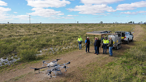 Drone sitting our on a dirt track road, with a group of 6 people standing near a ute and equipment near by. The group looks to be all talking amoungst themselves.