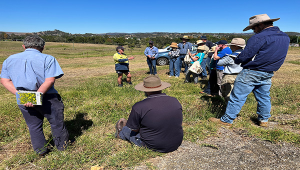 A group of people listening to a presenter in a paddock