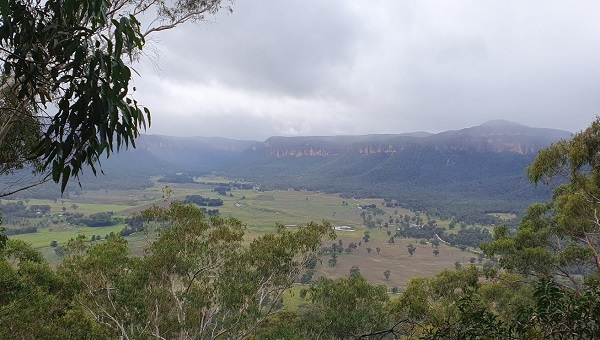 a senic shot of a green valley with sandstone escarpments in the background