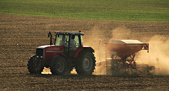 Tractor applying fertiliser to a dusty paddock