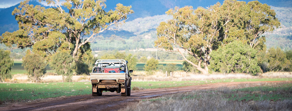 Landcruiser ute driving on a dirt road with a country landscape and sunset in the background. 