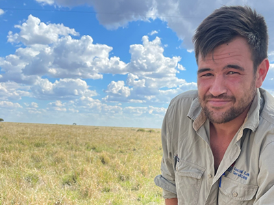 A man facing the camera with a paddock and blue sky in the background