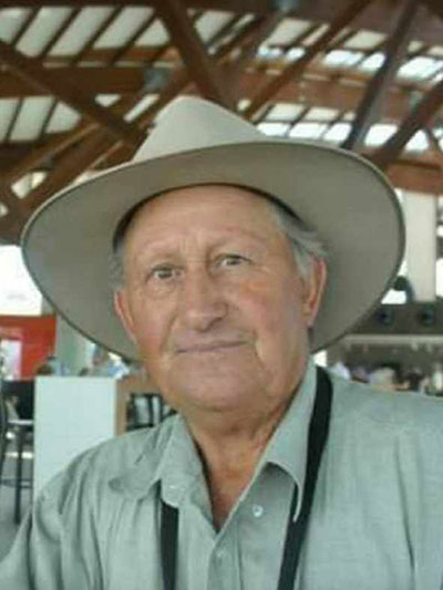 A man wearing a light coloured wide brim hat, slightly smiling at the camera
