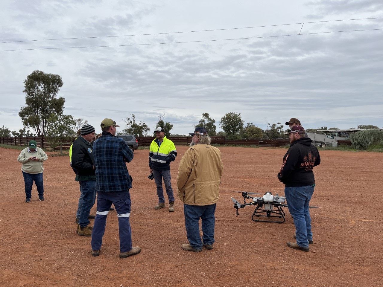 About 8 people standing as a group in a paddock with a drone next to the group.
